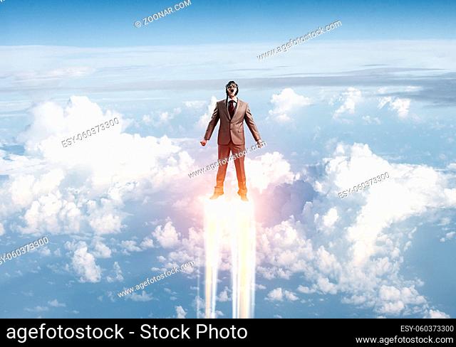 Businessman in suit and aviator hat flying in blue sky as superhero. Corporate manager as superman launching upwards with jet flame in stratosphere