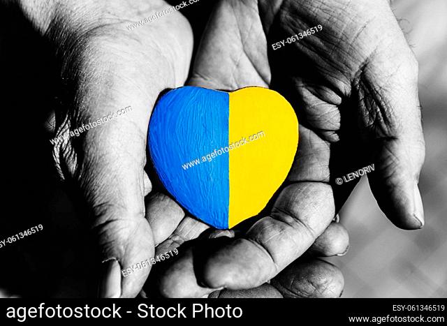 Senior man or soldier hands holding heart shape stone painted with Ukraine national flag colors. Pray for Ukraine, stop the war
