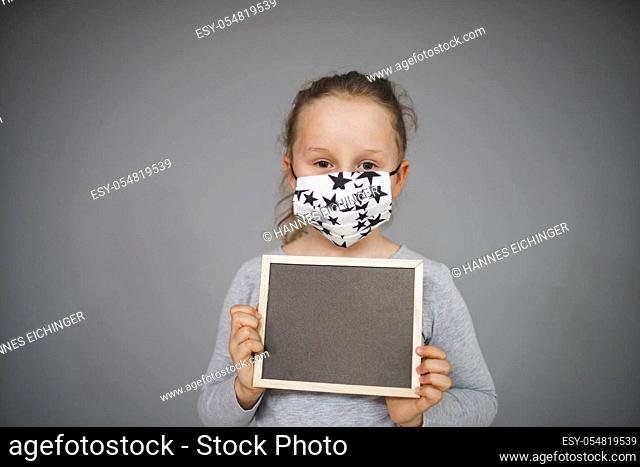 girl with message board and nose mouth mask is posing in front of grey background