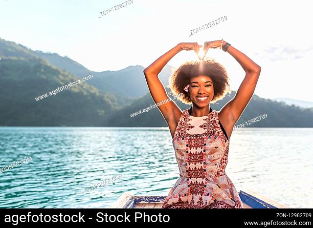 Afro american woman making heart with her hands on the boat. Very atmospheric photo. Woman is smilling with her whole face