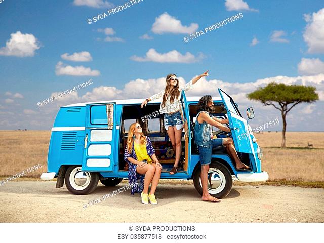 summer holidays, road trip, travel and people concept - smiling young hippie friends in minivan car over african savannah background