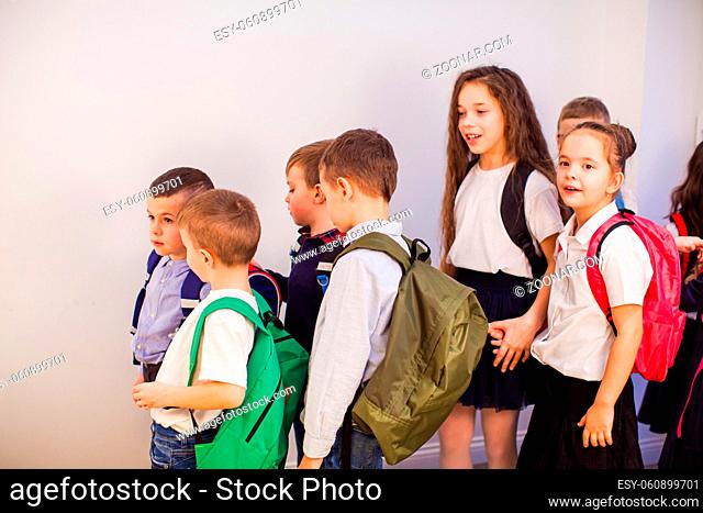 Group of happy little school kids in school. Children in uniform with backpacks in school corridor