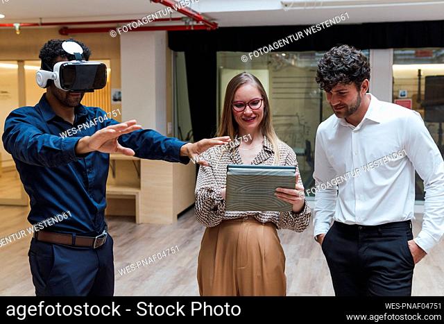 Businessman wearing VR goggles standing with colleagues in office