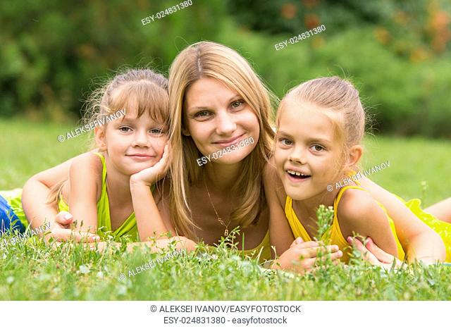 Mother and two daughters lie on the green grass, and looked into the frame