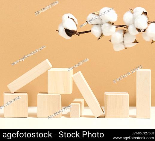 wooden cubes stacked and branches with white cotton flowers on a brown background. Podium for cosmetic products, beverages and food, eco products