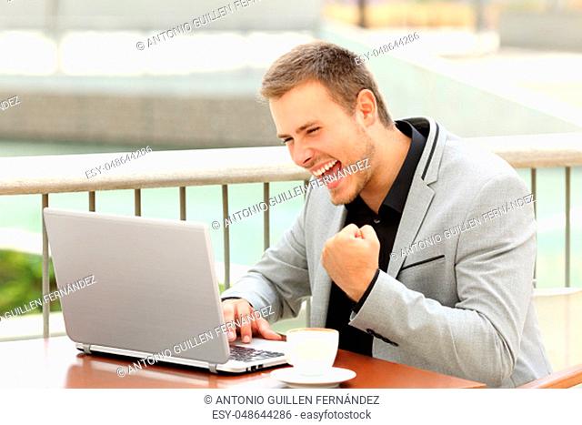 Excited executive reading good news on line in a laptop sitting in a coffee shop