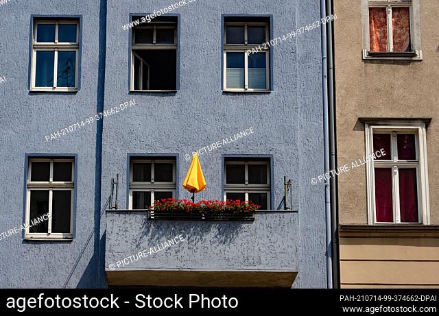 12 July 2021, Berlin: A yellow parasol stands on a balcony of a house on Karl-Marx-Strasse in Neukölln. The district continues to look for ways to positively...