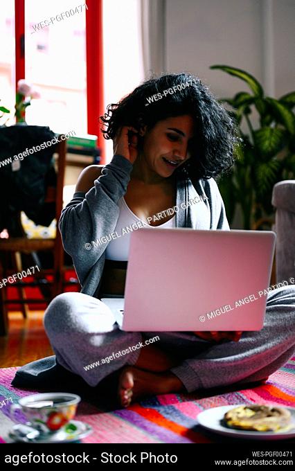 Woman with hand in hair using laptop while sitting on floor at home