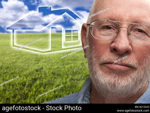 Melancholy senior man with green grass field and ghosted house behind him