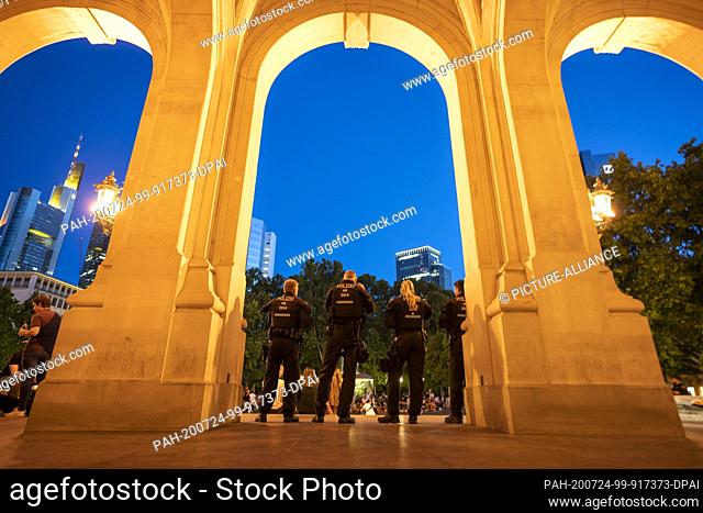 24 July 2020, Hessen, Frankfurt/Main: Policemen stand between the columns of the Alte Oper in the evening while people gather in front of the building to...