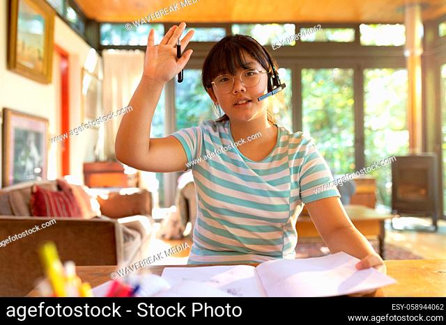 Asian girl wearing phone headset, raising hand during video call, learning online