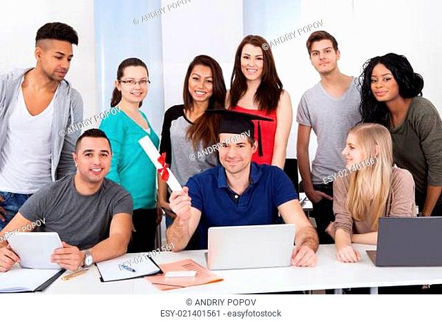 College Student Holding Degree With Classmates Looking At Him