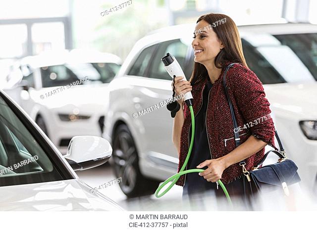 Smiling female customer carrying hybrid charging cable in car dealership showroom