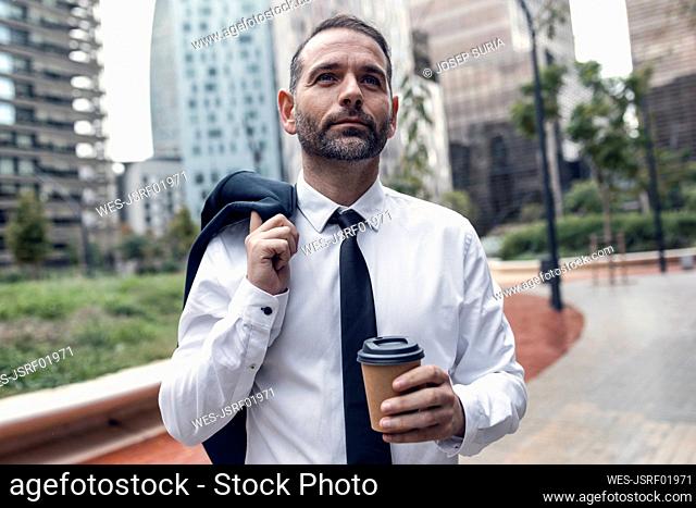 Portrait of businessman standing outdoors with jacket and disposable coffee cup in hands