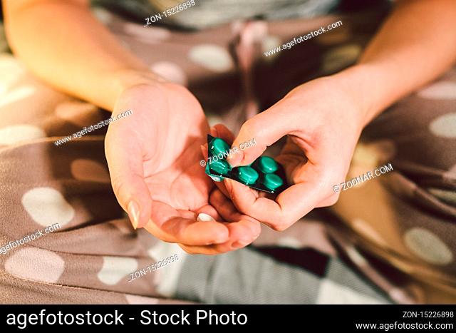Subject medicine health and pharmaceuticals. Close-up macro young caucasian woman hands pulling out a green blister. Packing two white round pills in home...