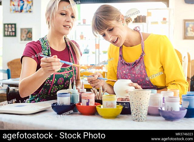 Two girl friends painting their own handmade ceramics in a hobby workshop