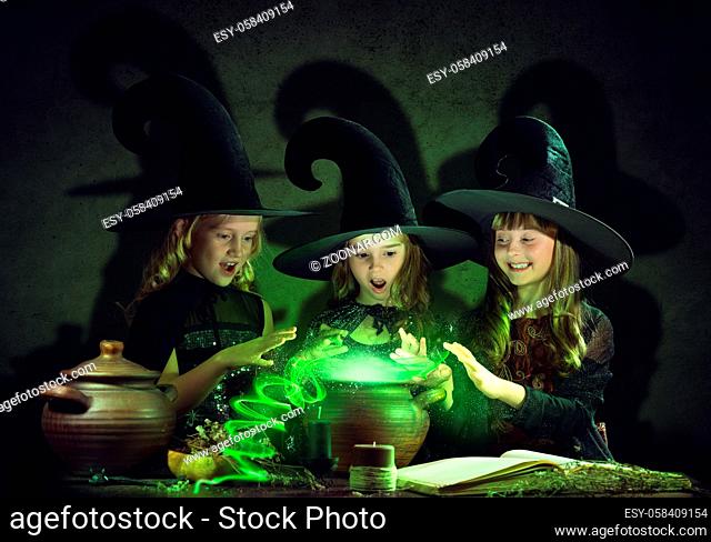 Three little Halloween witches reading conjure from magic book