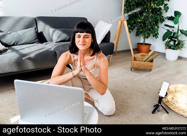 Smiling woman on video call with hands clasped sitting in front of laptop