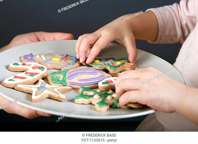 A mother sharing a plate of Christmas cookies with her daughter, focus on hands