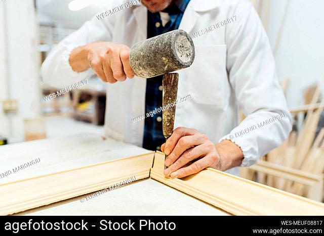 Hands of craftsman using work tool to make frame in workshop