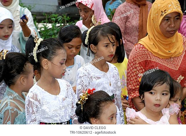 A group of 7 to12 year old Sasak girls wearing white embroidered blouses and flowers in their hair in Muslim Sasak wedding procession other girls and a woman...