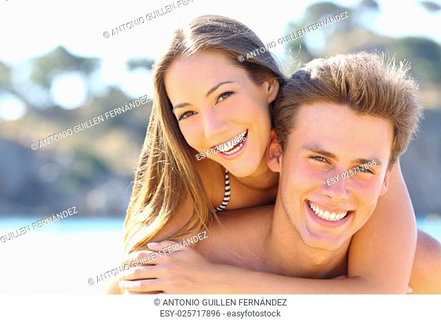 Happy couple with perfect smile and white teeth posing on the beach looking at camera