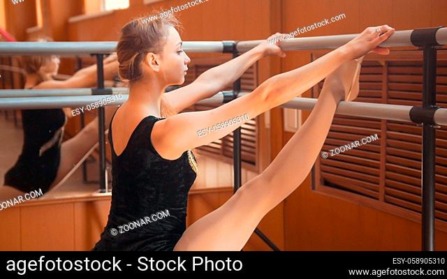 Young woman gymnast doing stretching leg on barre in a studio - close up