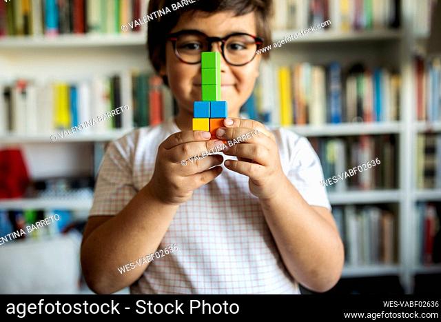 Smiling little boy with glasses playing with building blocks at home