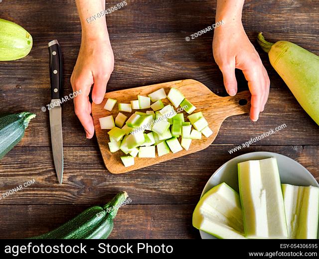 Zucchini harvest. Woman slices zucchini cubes for freezing on wooden table. Farm organic zucchini harvesting Top view or flat lay