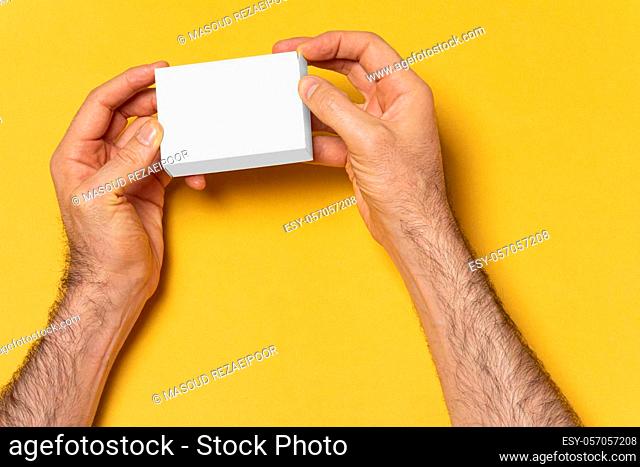 A man hands opening a small box in front of yellow background, editable mock-up series template ready for your design, box faces selection path included