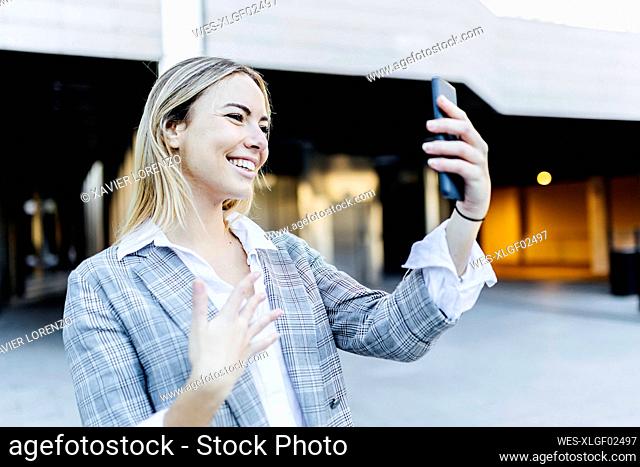 Happy blond working woman talking on video call through smart phone