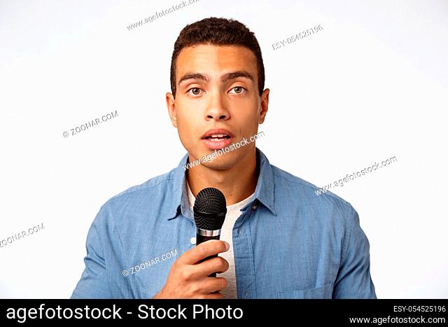 Cute romantic young caucasian guy confess love in front audience, holding microphone and talk with hopeful expression, standing white background, giving speech