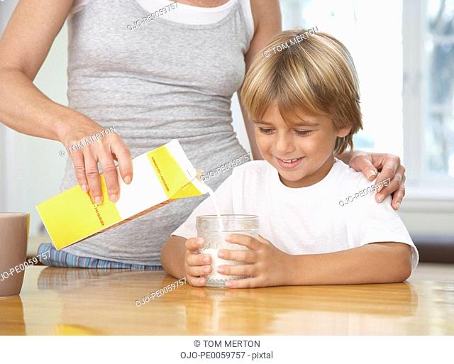 Woman in kitchen pouring young boy glass of milk