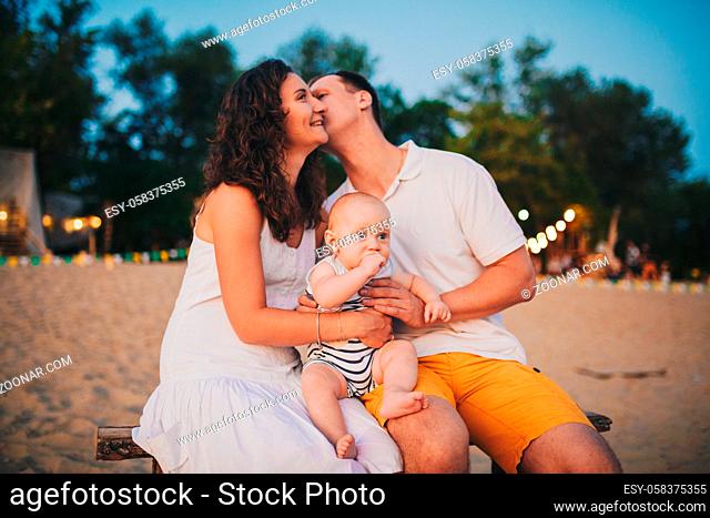 Theme family vacation in summer near the river. man and woman kiss, a small child son sitting on his hands with a funny emotion of surprise