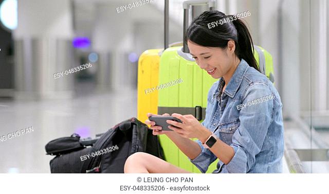 Woman use of cellphone with waiting for the flight transit at airport, sitting down on the floor with her luggage and backpack