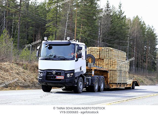 Salo, Finland - April 19, 2019: White Renault Trucks semi hauls a wide load of lumber on gooseneck trailer along highway on a day of spring