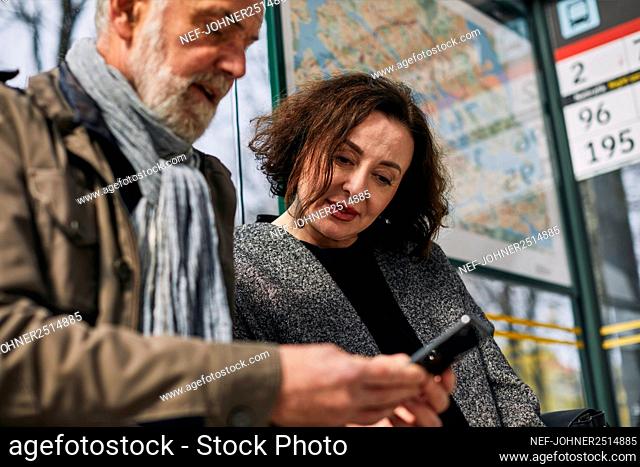 Mature couple using cell phone at bus stop
