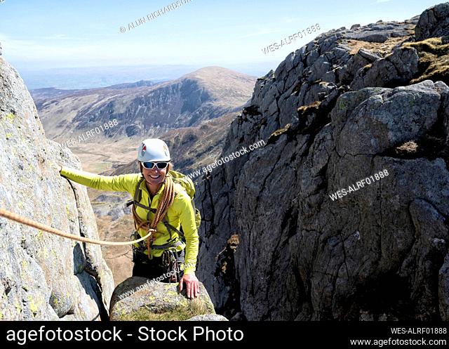 Smiling senior woman wearing helmet on rocky mountain peak