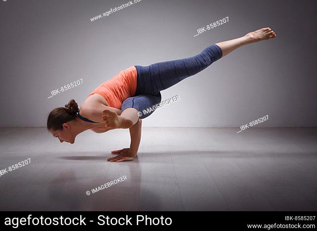 Beautiful sporty fit yogini woman practices yoga asana eka pada koundinyasana 1, pose 1 dedicated to sage Koundinya pose in studio
