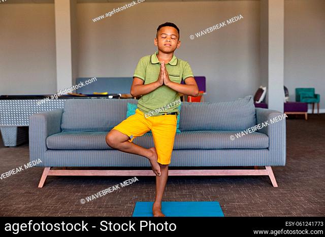 African american elementary boy with closed eyes standing on one leg while exercising in school