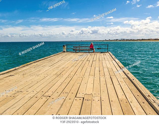 View to the end of the Frankston Pier, Melbourne, Australia. A woman sits on a bench watched the time come in