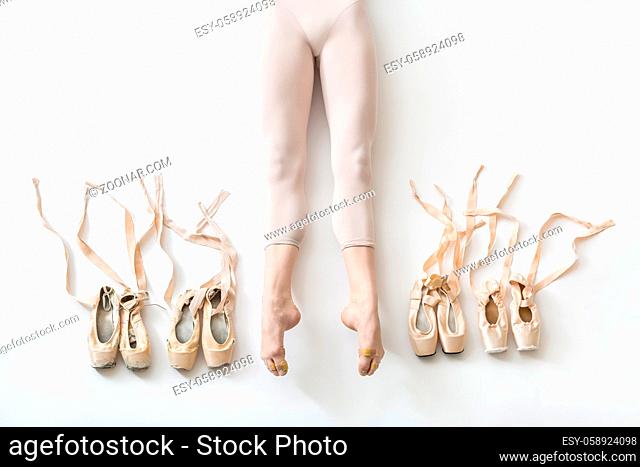 Gorgeous ballerina lies with stretched legs on the white floor in the studio. She wears a light dance wear. On the sides of her legs there are ballet shoes