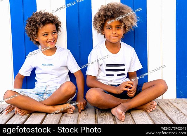 Smiling brothers sitting on wooden walkway against striped wall