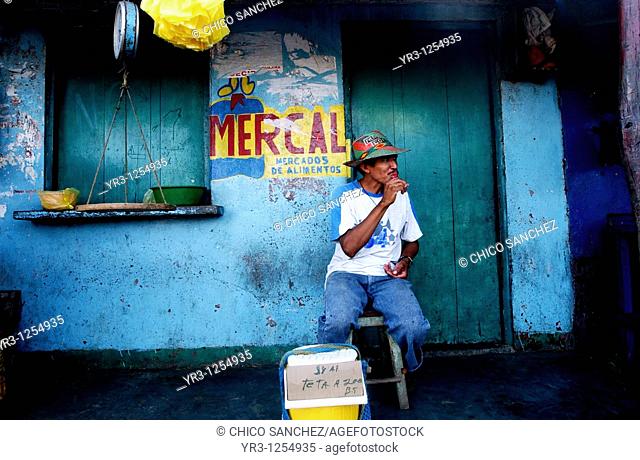 A candy vendor sits outside a closed state-run grocery store called Mercal in Paraguaipoa, Venezuela