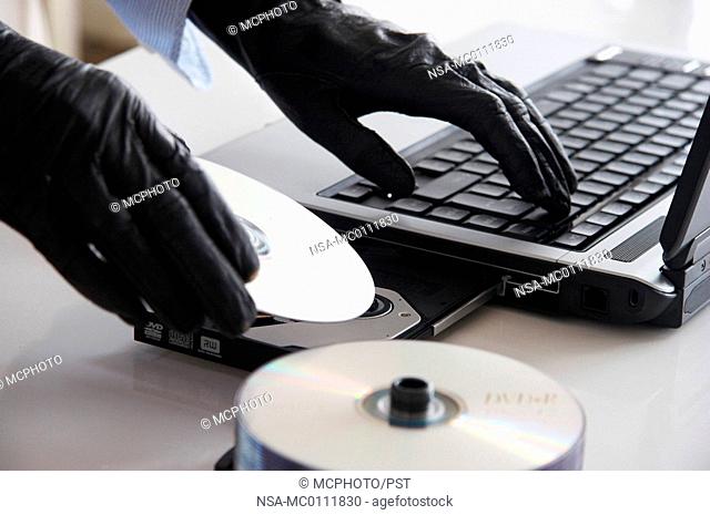 gloved hands, a laptop and some discs