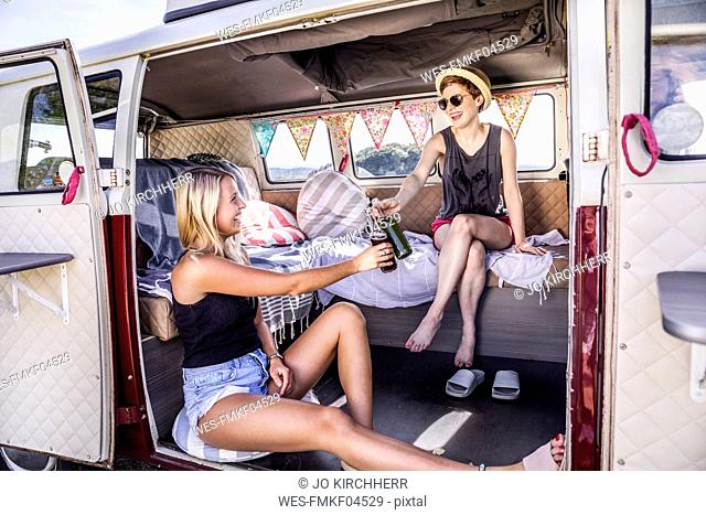 Two happy women inside van clinking bottles