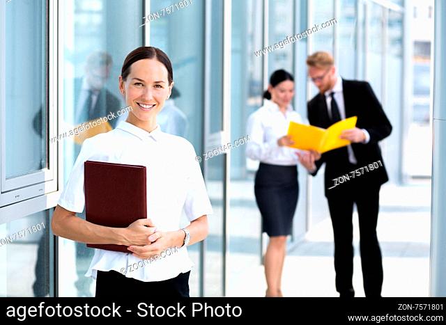 Attractive young businesswoman smiling isolated on her collegues. Woman in white shirt posing with documents in her hand