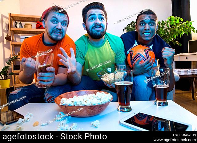 Low view of best friends gather together for watching football game on TV. Handsome men drinking alcohol drinks and eating pop corn