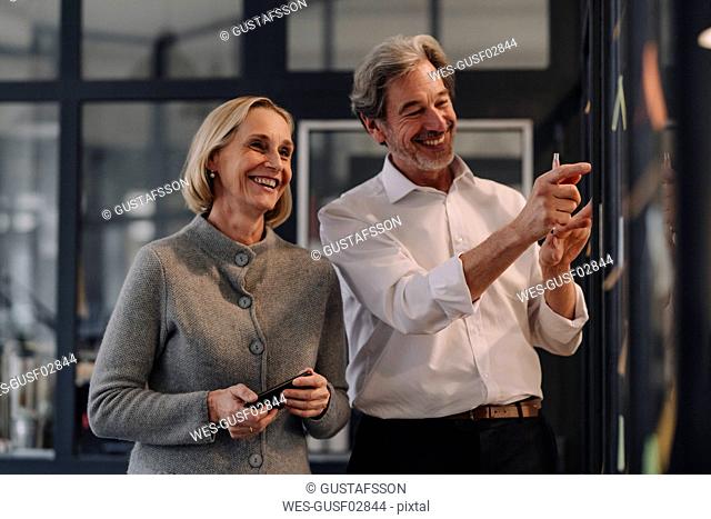 Happy businessman and businesswoman working on sticky notes at glass pane in office