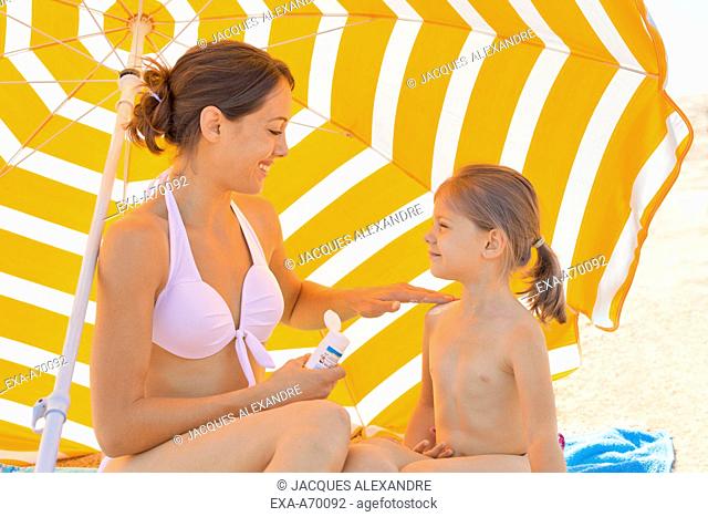 mother with baby under parasol at beach, sun creme